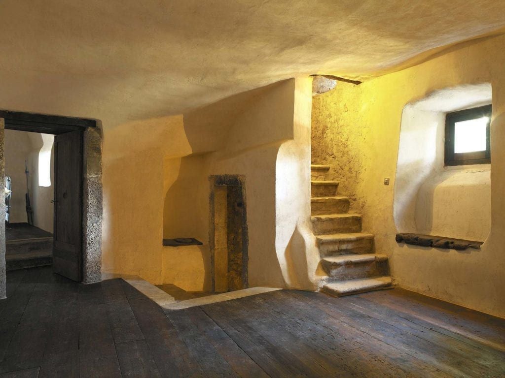 Rustic Italian stone bedroom with handcrafted wooden furniture, soft linens, and warm natural light in a historic Abruzzo mountain village hotel room