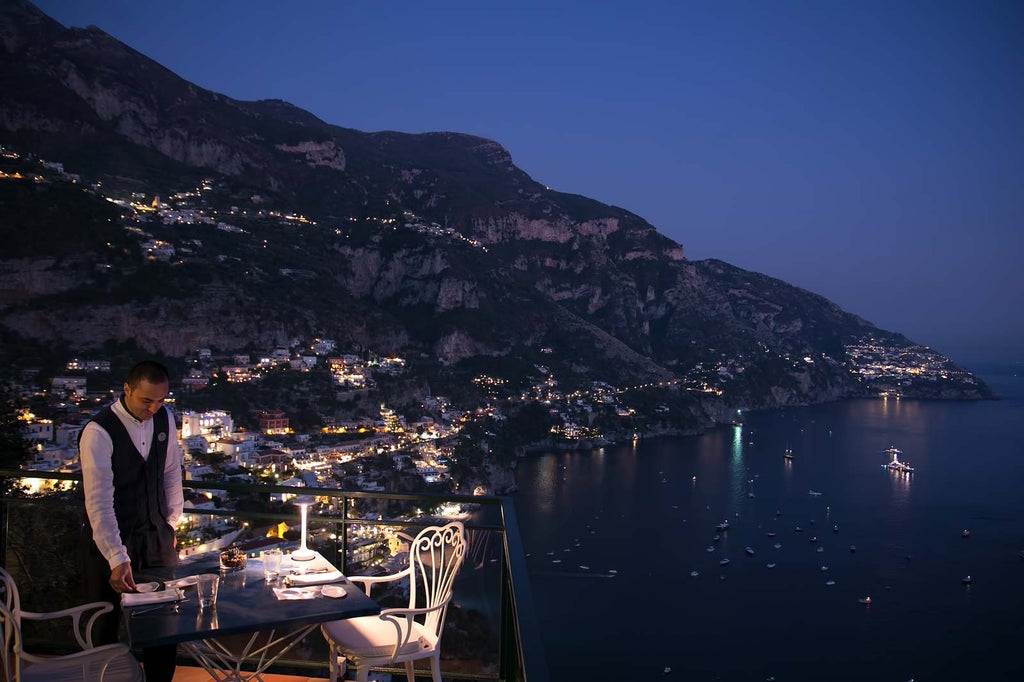 Luxurious cliffside hotel with cascading white terraces overlooking the Amalfi Coast, surrounded by Mediterranean vegetation and blue sea