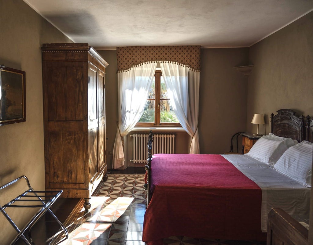 Elegant classic hotel room with white linens, rustic wooden furniture, and soft natural light, showcasing Sicilian countryside view through large window