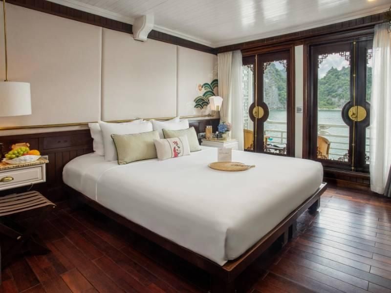 Elegant executive cabin on Bhaya Cruises, featuring rich wood paneling, plush white bedding, and panoramic views of Vietnam's scenic halong bay