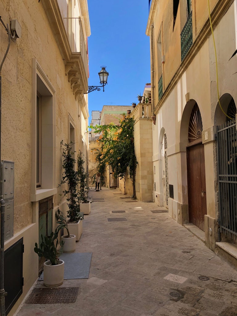 Whitewashed Italian villa in Puglia with rustic stone walls, arched doorway, and lush potted plants under a deep blue summer sky