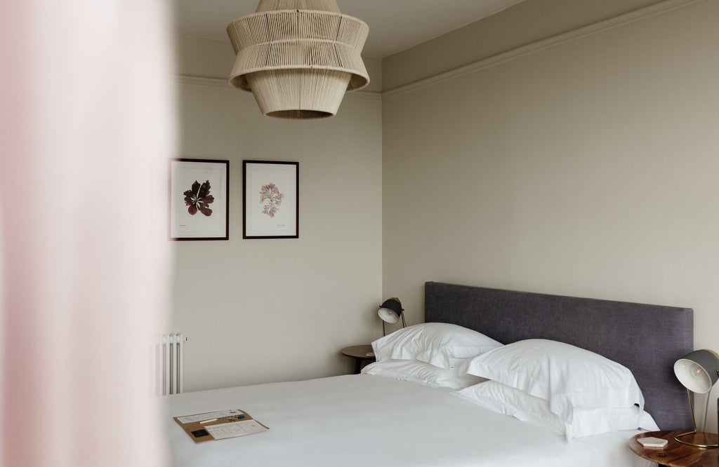 Elegant coastal-inspired bedroom with plush white bedding, nautical blue accents, and large window overlooking serene UK landscape at The Sandy Duck hotel