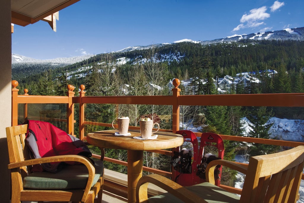 Elegant mountain resort with stone facade, glass windows, and snow-capped peaks behind lit by warm evening light in Whistler, Canada