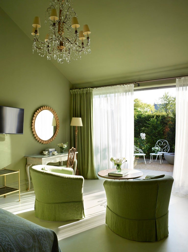 Elegant garden-inspired bedroom with soft sage green walls, plush white bedding, and rustic wooden furniture at a luxurious UK countryside hotel