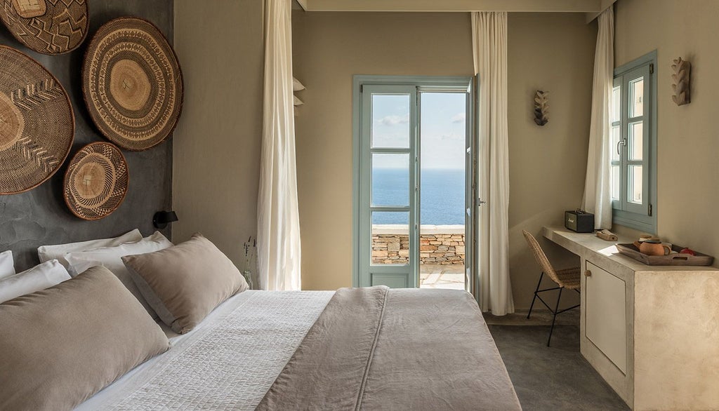 Minimalist white bedroom with sea-view terrace at Verina Astra hotel, featuring crisp linens, modern decor, and panoramic Aegean coastline in Sifnos, Greece