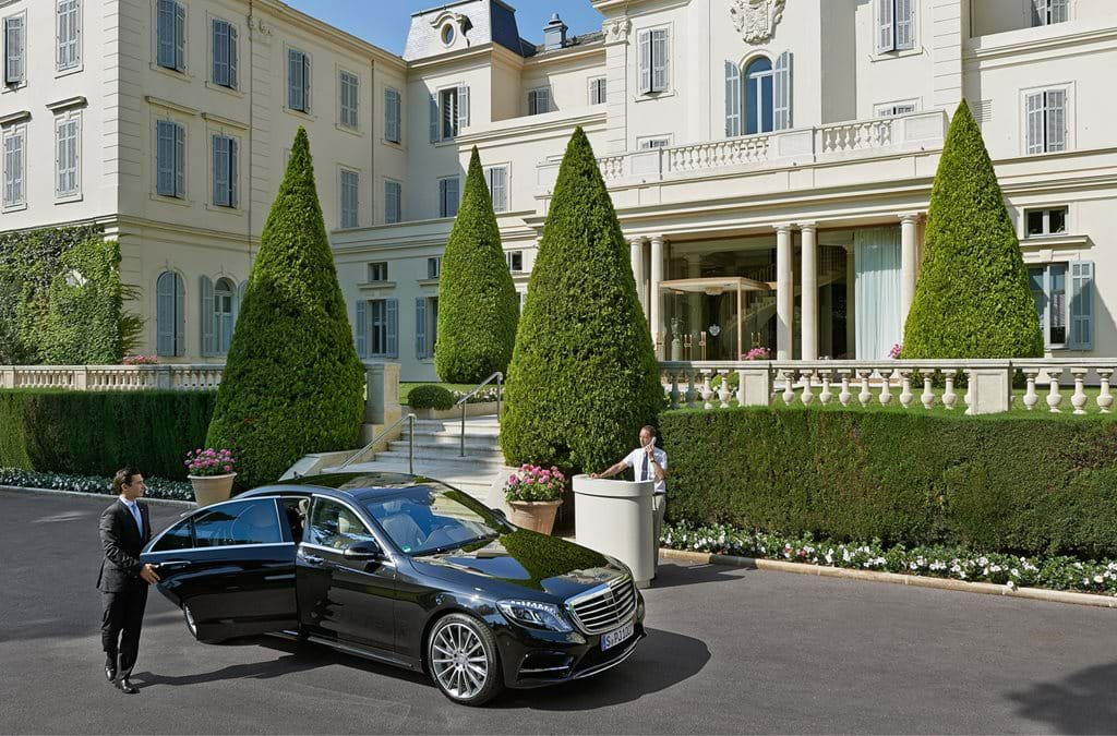 Elegant cliffside luxury hotel in French Riviera with grand white facade, manicured gardens and infinity pool overlooking Mediterranean Sea