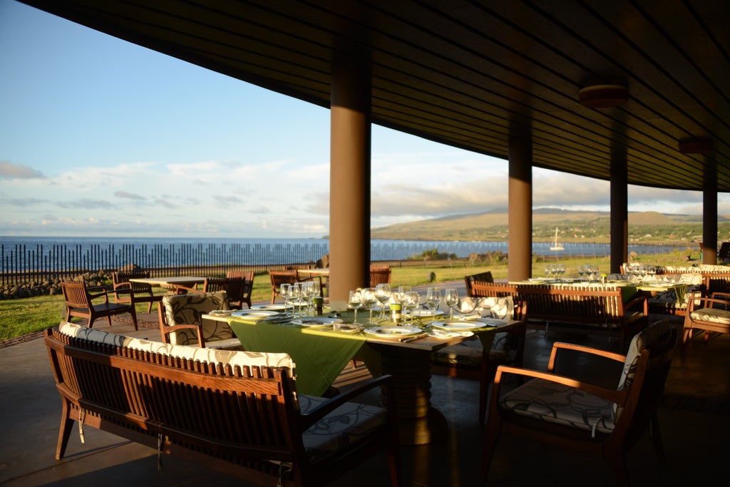 Modern luxury resort with curved stone buildings nestled into green hillside overlooking Pacific Ocean, Easter Island landscape