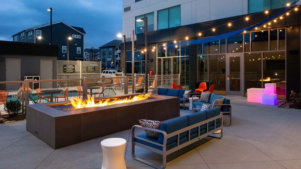 Modern, sleek hotel exterior with glass facade, illuminated at night, situated near airport with urban skyline, reflecting contemporary architectural design of Scenset property