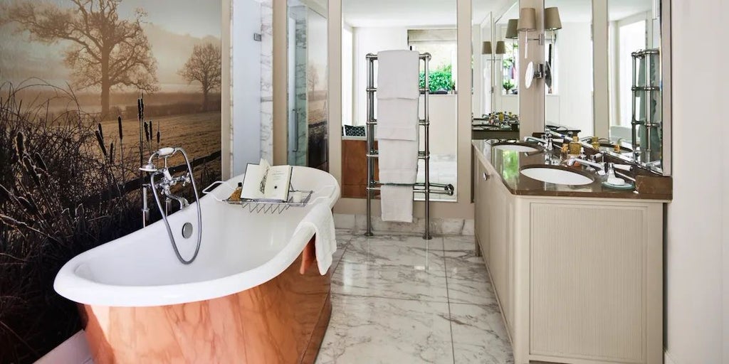 Elegant Gardener's East Cottage Suite at Coworth Park, featuring plush white bedding, rustic wooden furnishings, and soft natural light through large windows