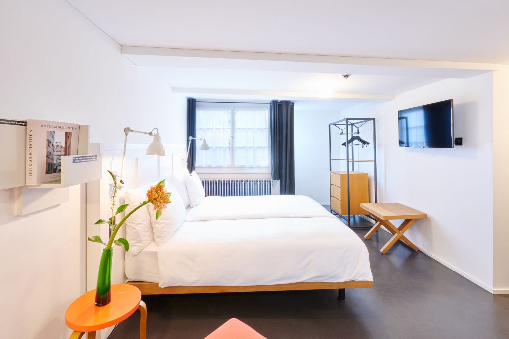 Modern Swiss hotel room with elegant wood furnishings, crisp white linens, large window overlooking urban scenery, minimalist design with warm neutral color palette