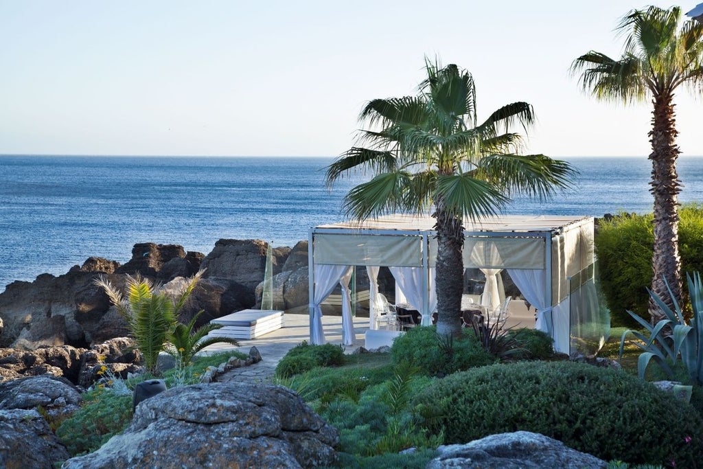 Luxurious white coastal hotel with blue-tiled roof overlooking rocky Cascais shoreline, elegant architecture blending traditional Portuguese design with modern sophistication