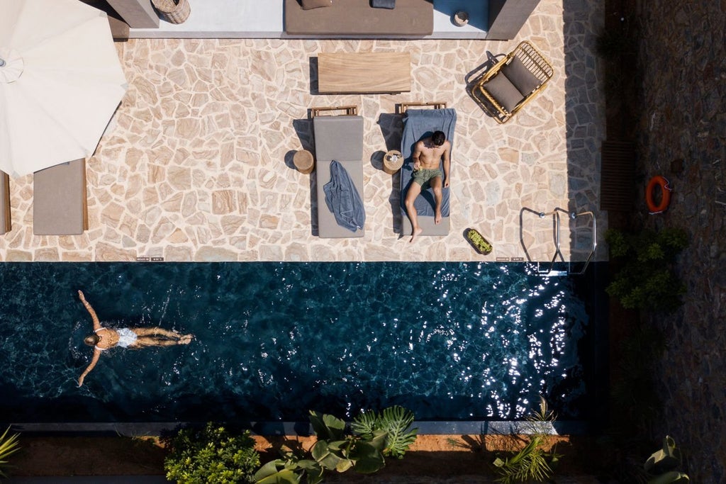 Modern Mediterranean resort nestled in hillside with infinity pools, private cabanas, and panoramic views of Cretan coast at sunset