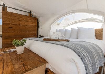 Luxurious canvas tent with large stargazing window overlooking dramatic Zion landscape, featuring king-sized bed and rustic modern glamping interior design