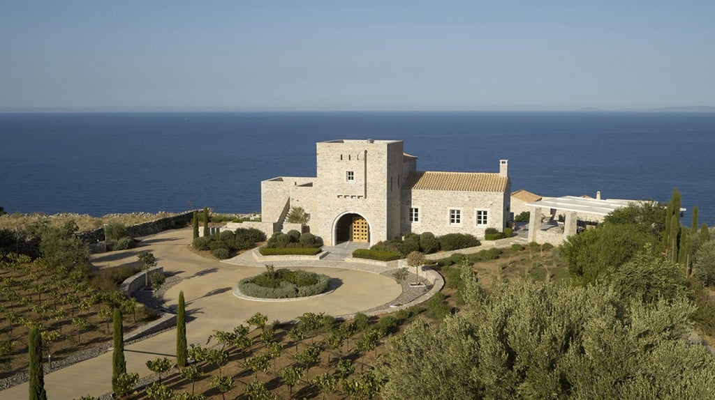 Elegant stone villa nestled in lush Greek landscape, traditional architecture with terracotta roof overlooking azure Mediterranean coastline at golden hour