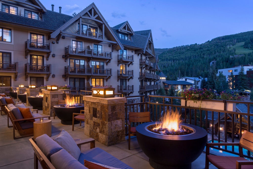 Grand Four Seasons Vail resort nestled against snow-capped mountains, featuring stone facade, timber accents and manicured gardens