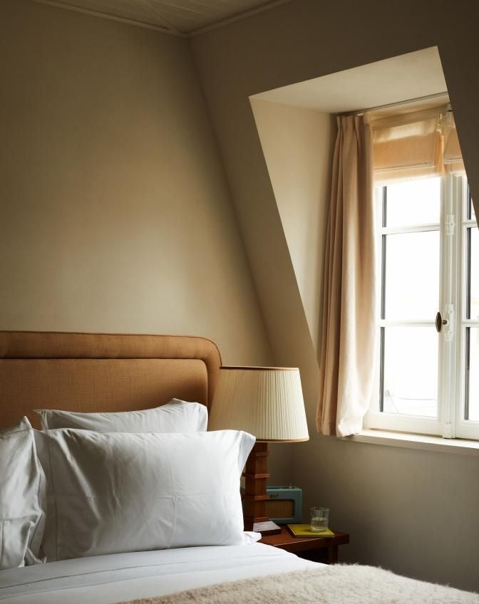 Elegant Parisian hotel suite with plush cream-colored armchair, rich wooden floors, tall windows, and opulent gold-framed artwork in soft neutral tones