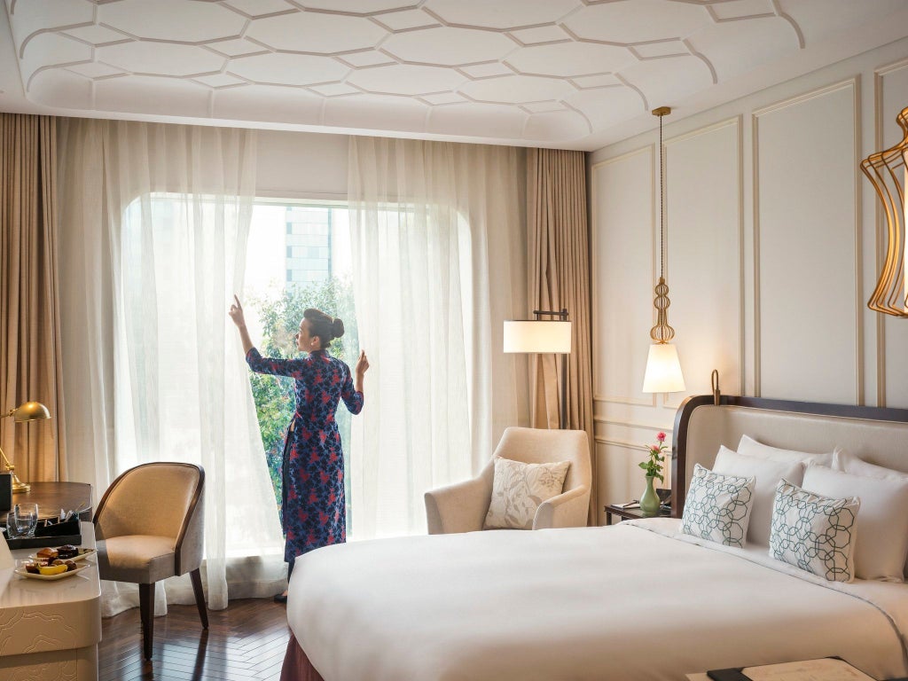 Contemporary luxury hotel room with king bed, floor-to-ceiling windows, elegant furnishings, and panoramic Saigon city views