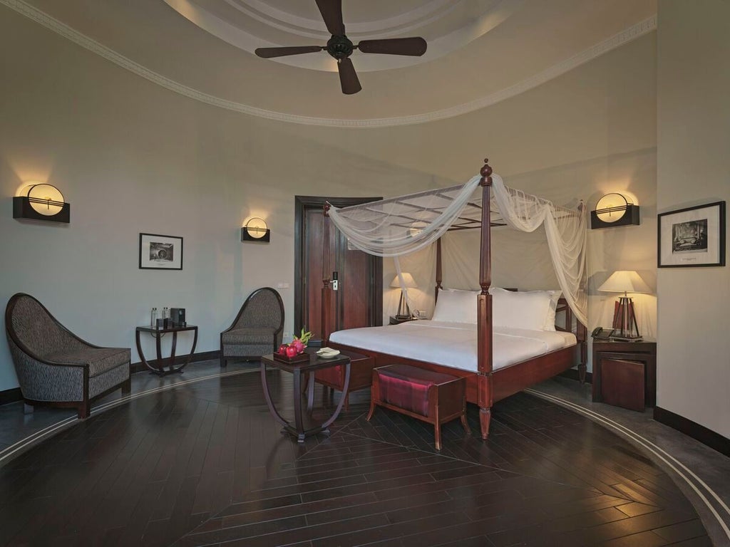 Elegant colonial-style junior suite with polished wood floors, plush white bedding, and traditional Vietnamese architectural details in warm, rich tones