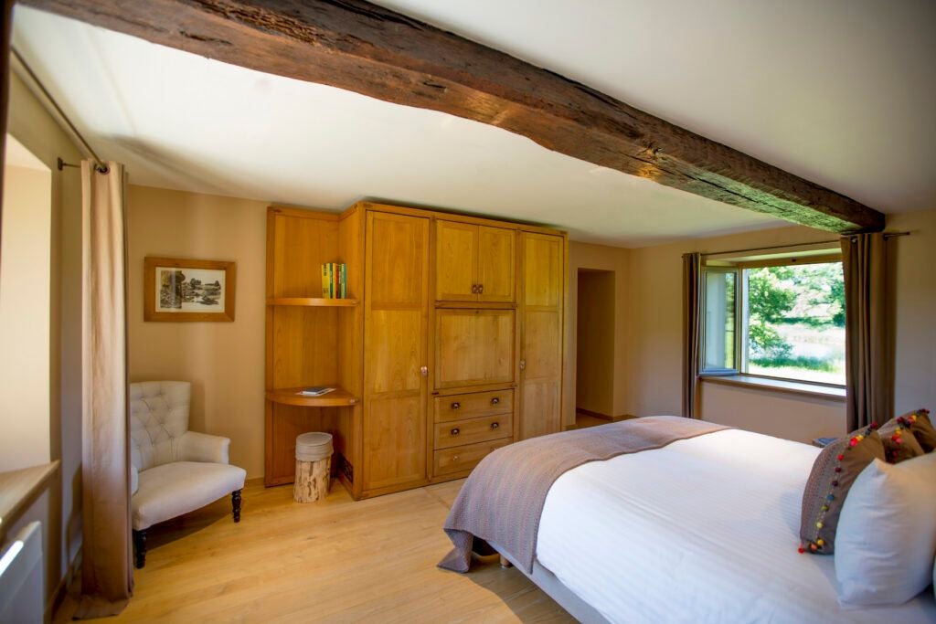 Luxurious French countryside bedroom with elegant wooden furnishings, soft neutral tones, and large windows overlooking lush green landscape at Domaine des Etangs