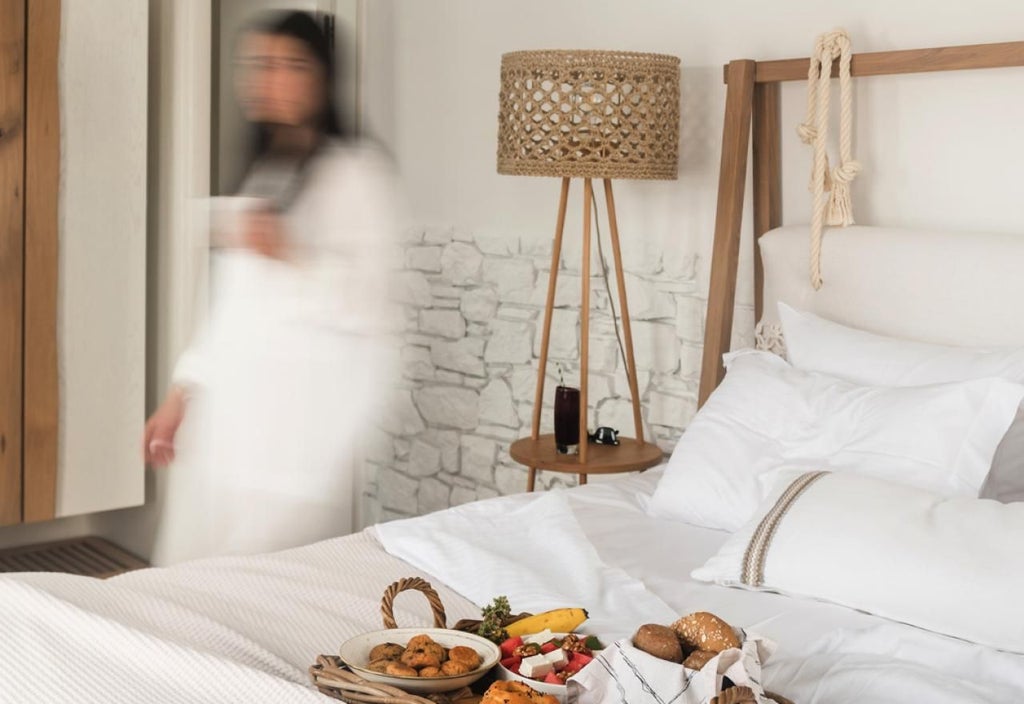 Elegant honeymoon suite with white-washed walls, arched windows overlooking Aegean Sea, minimalist decor, and a plush king-size bed in scenic Greece