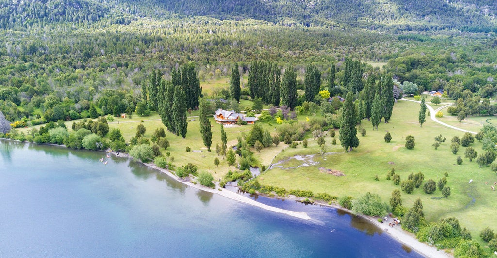 Luxurious lakeside lodge in Patagonia with stone facade, wooden beams, and panoramic windows reflecting mountain and water views