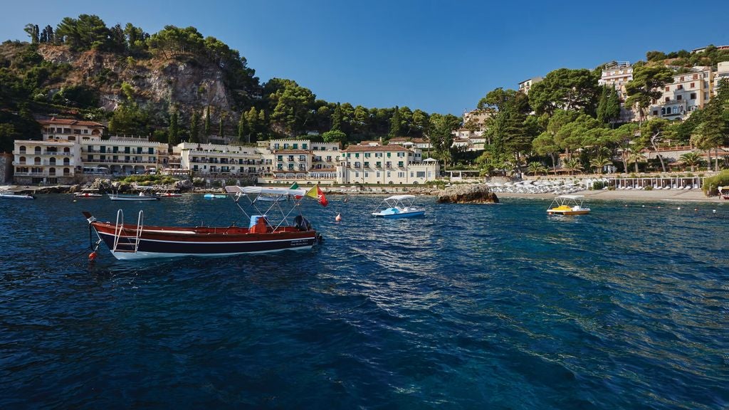 Elegant seaside hotel with private beach, Mediterranean architecture nestled into Sicily's coastline beneath Taormina's cliffs