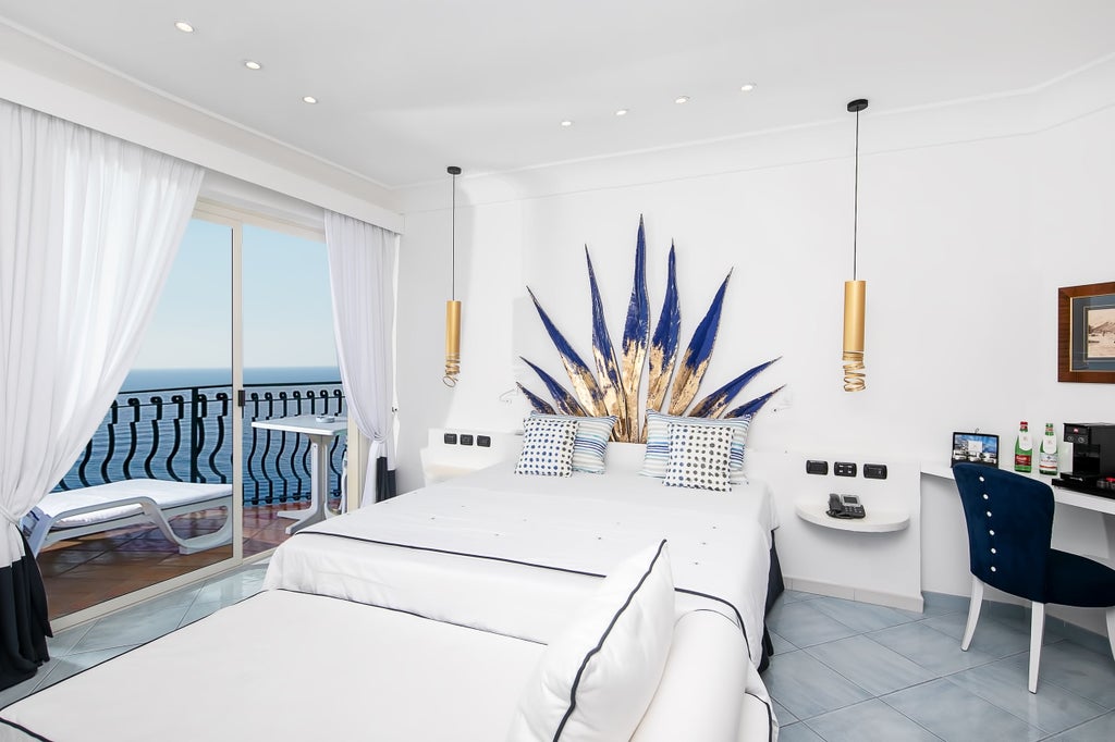 Elegant coastal hotel room with private balcony, featuring modern decor, white linens, and panoramic Mediterranean Sea views through glass doors