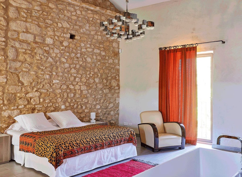 Elegant stone-walled suite with antique furnishings, soft cream linens, and rustic French provincial charm at a boutique hotel in southern France