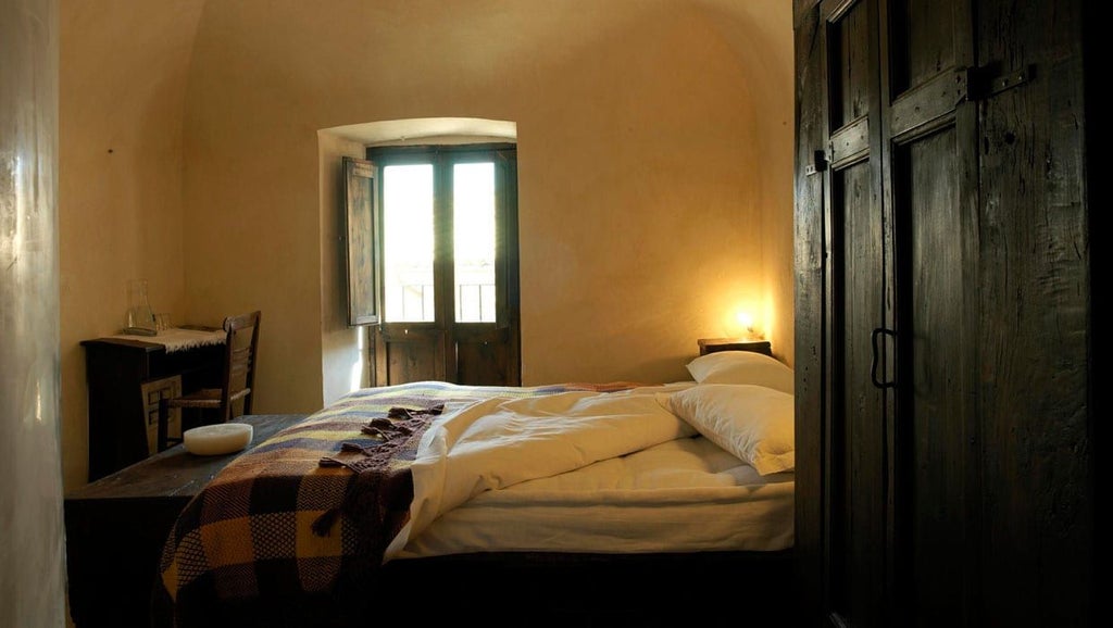 Rustic Italian hotel room with stone walls, wooden furnishings, and a charming balcony overlooking medieval Santo Stefano di Sessanio landscape