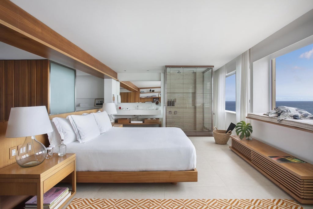 Elegant modern hotel room with panoramic ocean view, minimalist Brazilian design, soft neutral tones, sleek furniture, and expansive floor-to-ceiling windows overlooking Rio's coastline