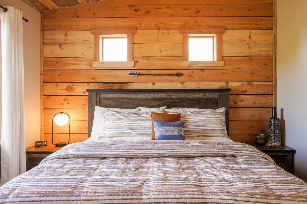 Rustic wooden lodge bedroom with plush king bed, panoramic mountain views, warm earth tones, and elegant southwestern-inspired decor in United States.