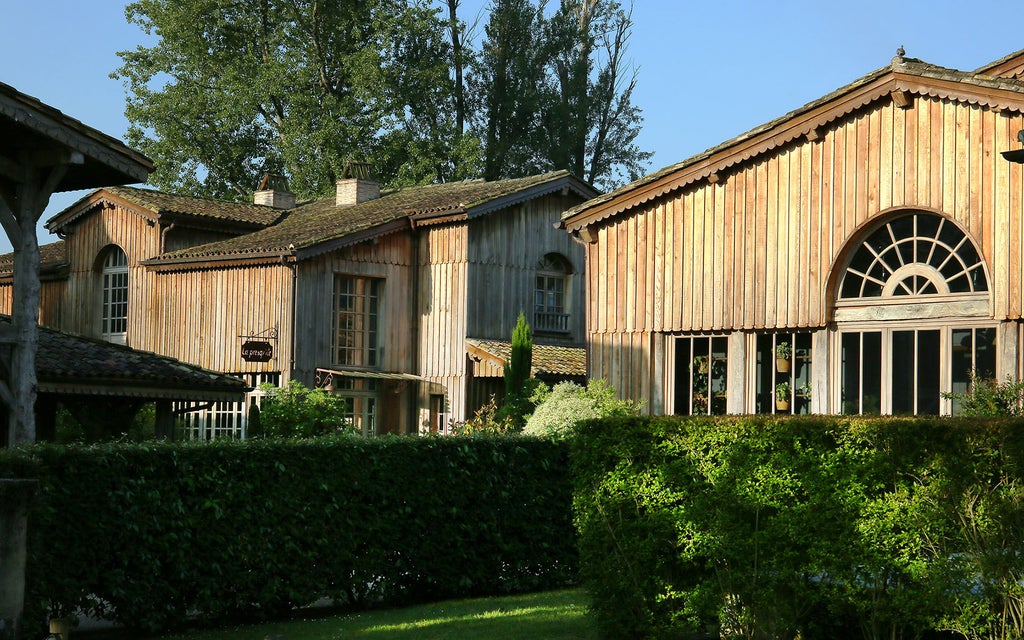 Elegant French vineyard hotel with rustic stone facades, wooden balconies, and tranquil lake reflections amid lush gardens at dusk