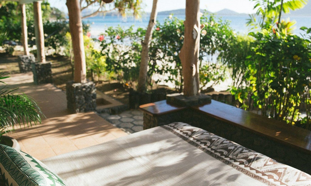 Luxurious Fijian water's edge villa with teak wood deck, infinity pool overlooking turquoise ocean, and lush tropical landscape at sunset