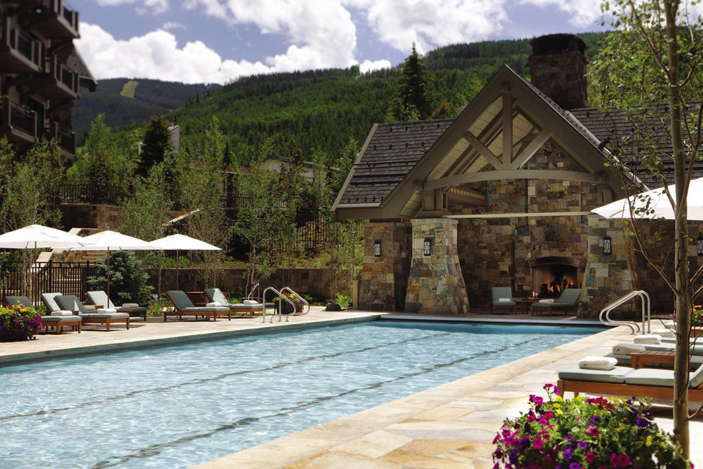 Elegant stone facade of mountain resort hotel with dramatic peaked roofs, surrounded by pine trees and snow-covered slopes in Vail