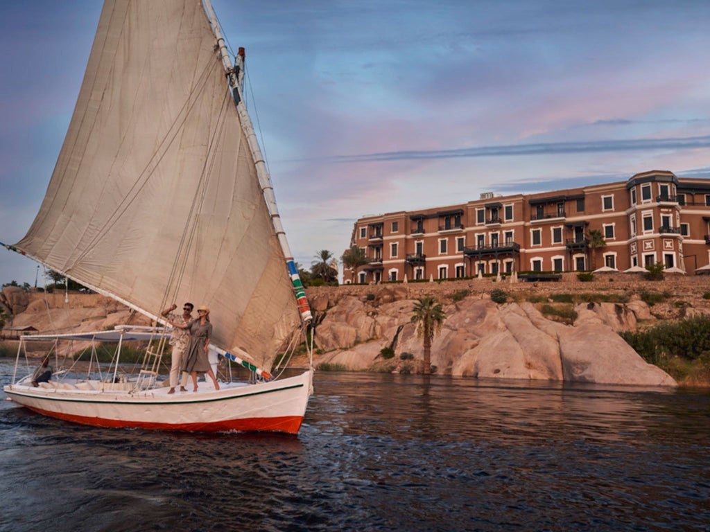 Luxurious Sofitel Legend Old Cataract Aswan hotel nestled on Nile riverbank, with elegant colonial architecture and panoramic desert landscape backdrop