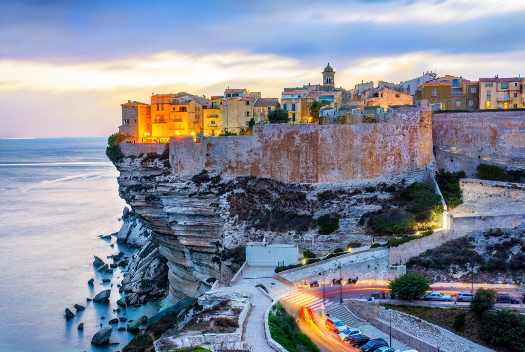 Beach town of Calvi in Corsica with historic citadel perched on rocky promontory, turquoise Mediterranean waters, and luxury yachts in harbor