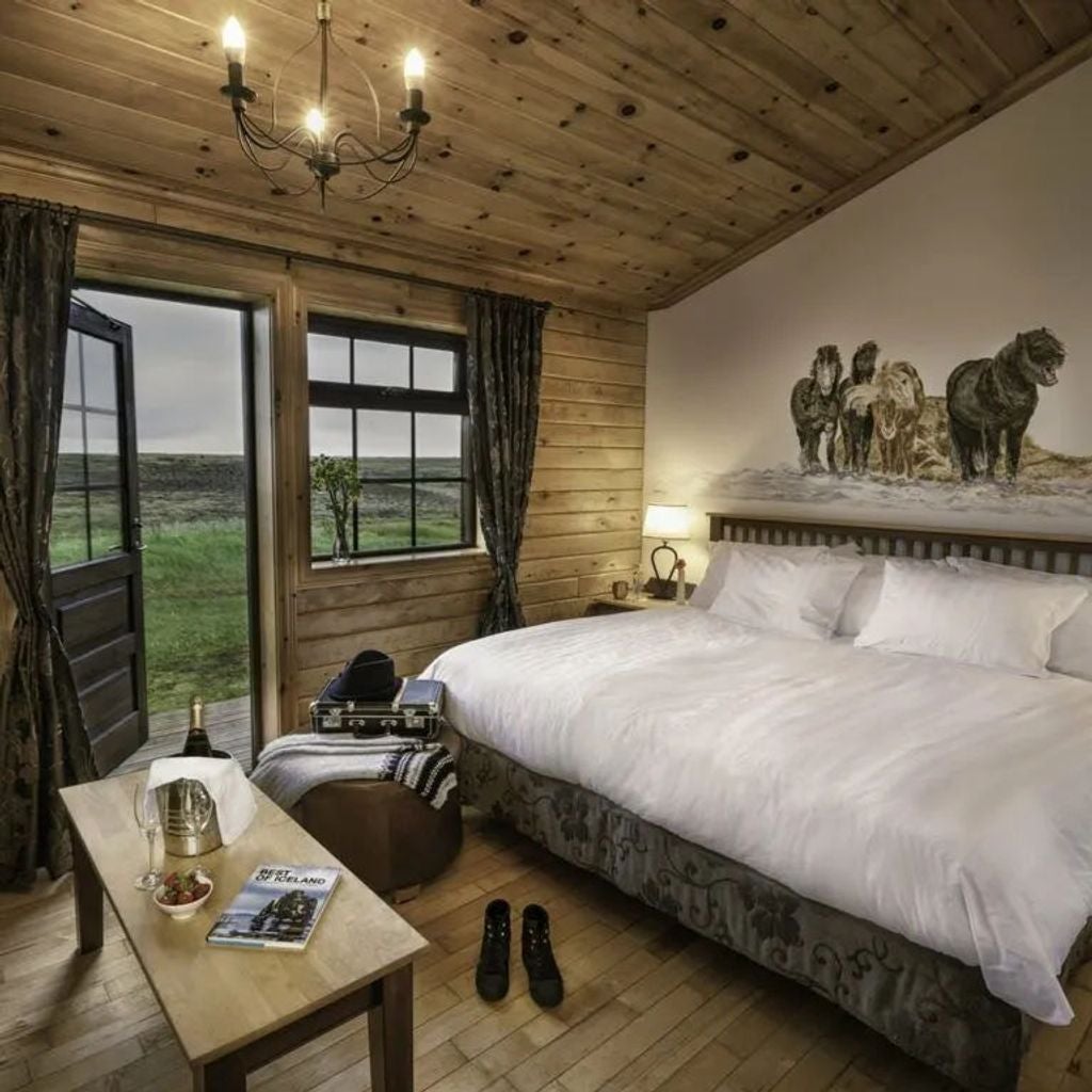 Cozy deluxe room with rustic wooden decor, plush king bed, floor-to-ceiling windows offering stunning views of Icelandic landscape