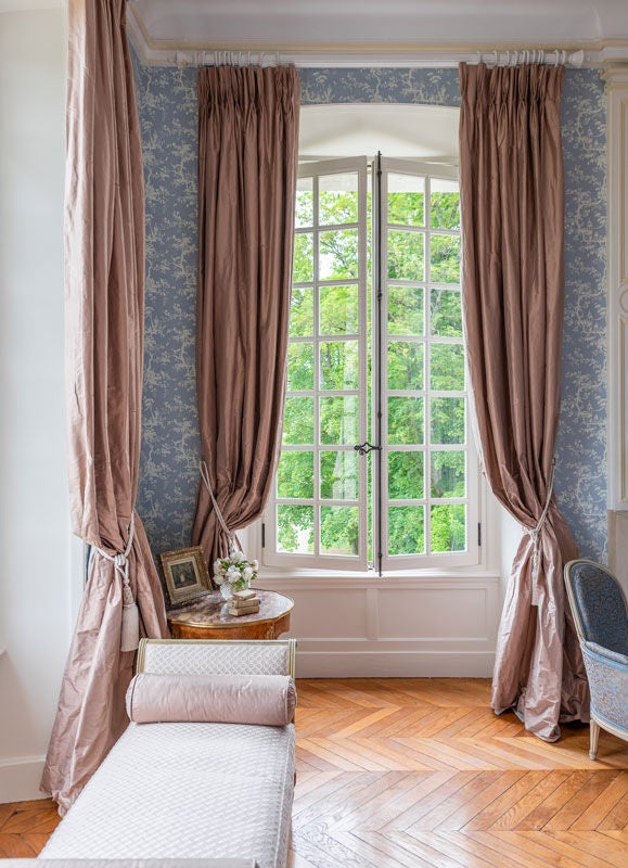 Elegant corner king room with tall windows, antique furnishings, and garden views in a French château, featuring ornate crown molding