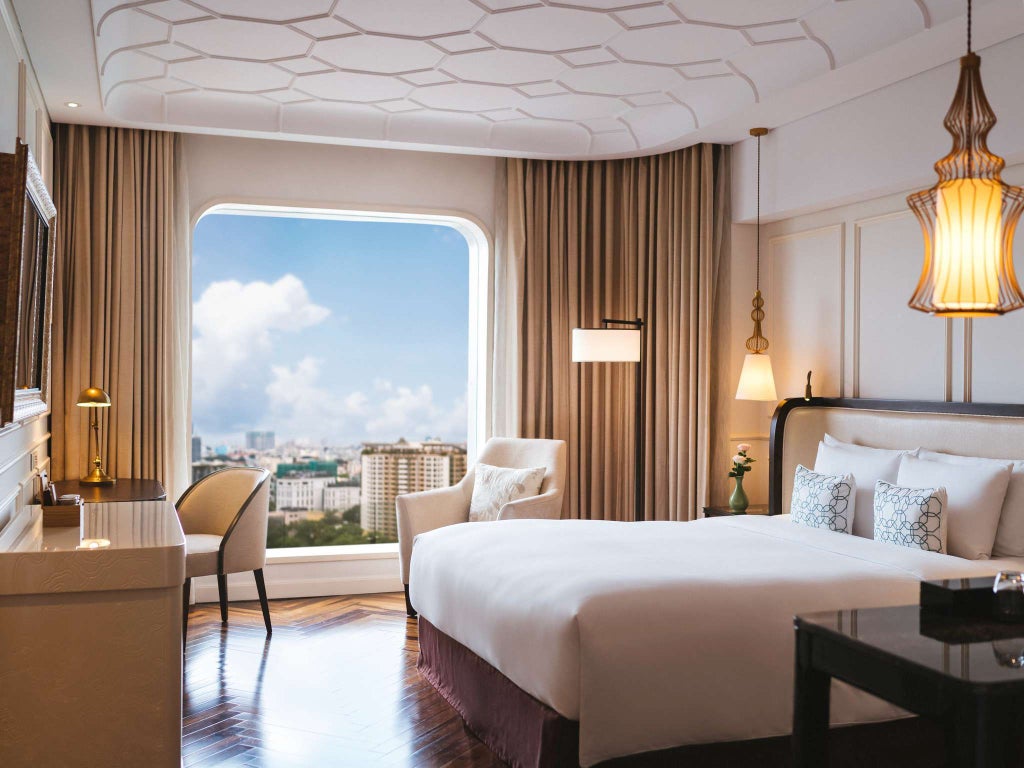 Elegant king hotel room with floor-to-ceiling windows, modern décor, plush white bedding, and city views of Ho Chi Minh City skyline