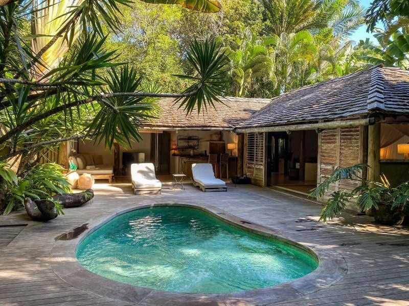 Rustic wooden bed with white linens in a tropical Brazilian hotel room, featuring natural textures, warm lighting, and minimalist decor at a luxurious spa resort