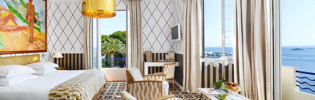 Elegant hotel room with a private terrace overlooking the French Riviera coastline, featuring Art Deco furnishings and panoramic sea views