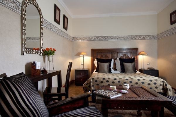 Luxurious Moroccan hotel suite with private terrace, featuring ornate tile work, plush seating, and traditional lanterns overlooking courtyard