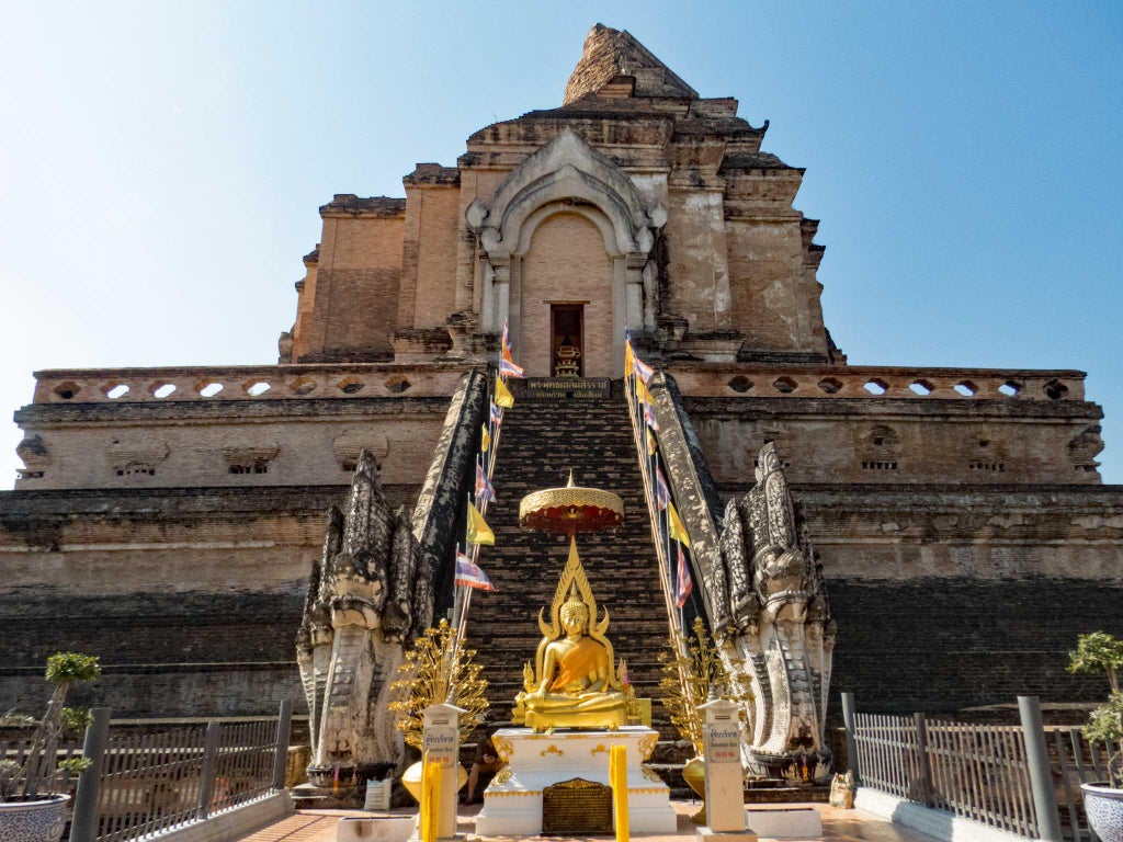 Ornate golden temple spires rise above lush tropical trees in Chiang Mai, Thailand, under a vibrant blue sky with white clouds