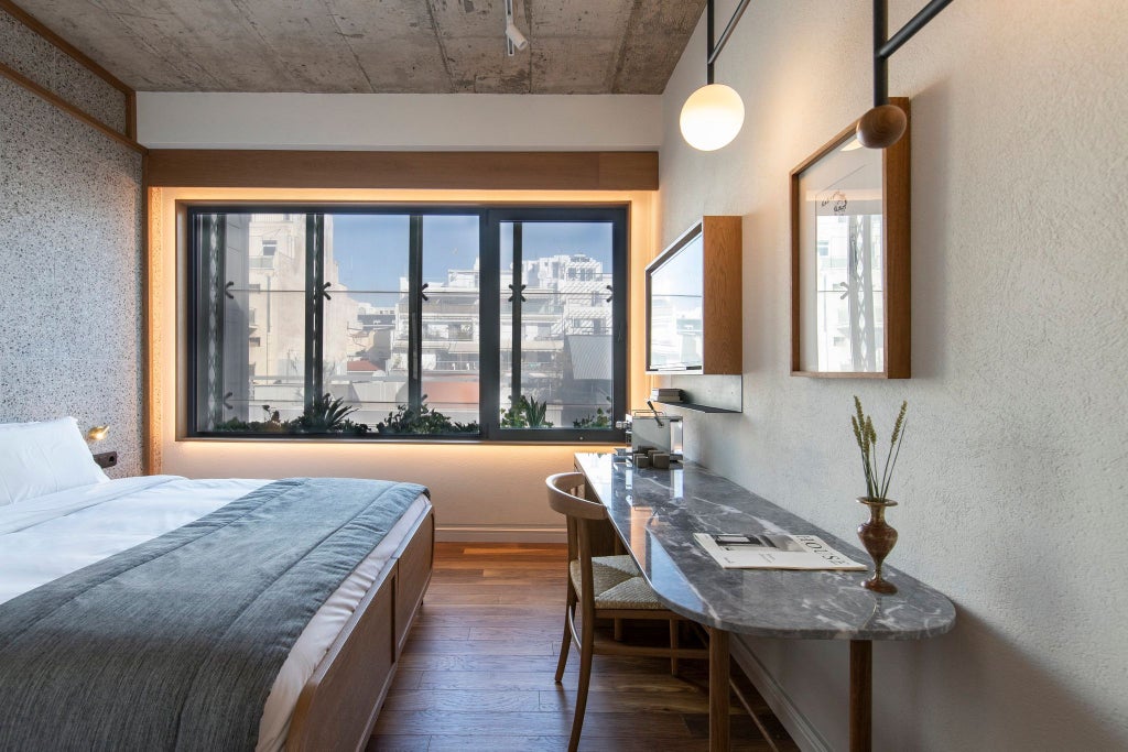 Minimalist hotel room with warm wooden accents, crisp white linens, and soft grey walls, showcasing contemporary Greek design in Ergon House Athens.