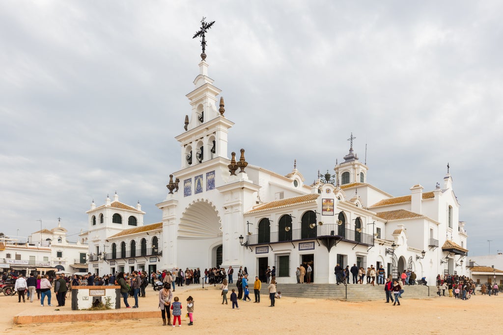 Vibrant Spanish pilgrimage scene at El Rocio, with traditionally dressed devotees on horseback, white-washed buildings, and colorful religious procession