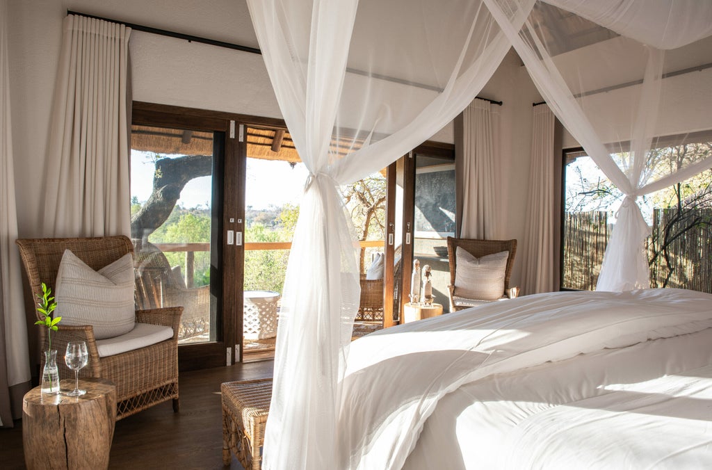 Luxurious safari lodge with thatched roof and wooden deck overlooking a pristine African savanna dotted with acacia trees at sunset