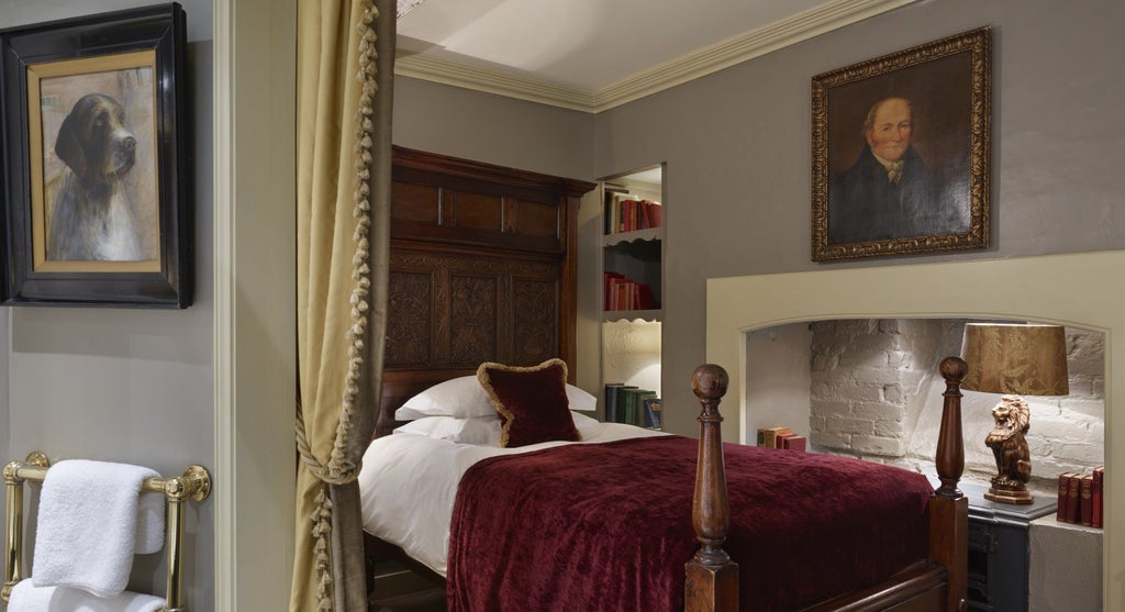 Elegant British-style single hotel room with rich wooden furnishings, plush burgundy accents, classic artwork, and sophisticated period-inspired decor at a luxury boutique establishment