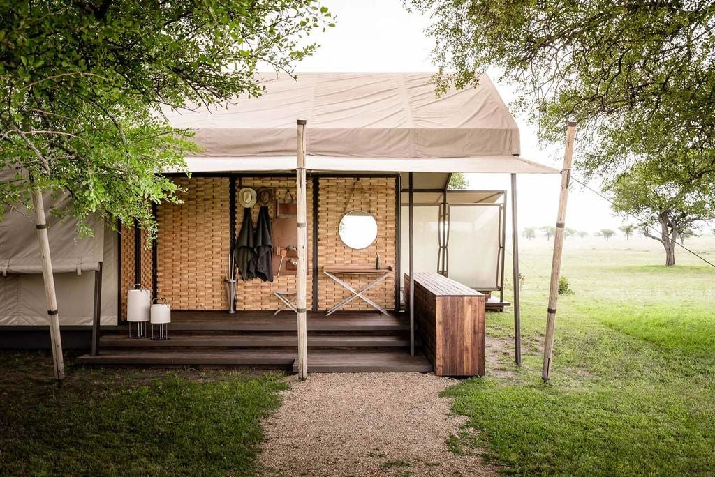 Luxurious safari tent with private deck overlooking Serengeti plains, featuring elegant colonial furnishings and canvas walls