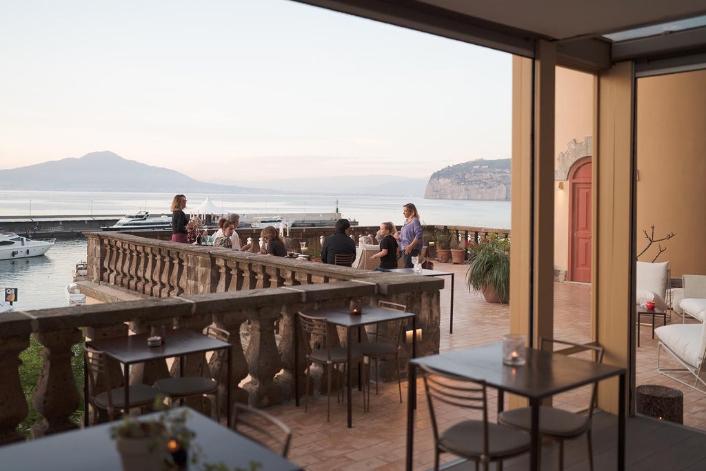 Elegant waterfront hotel with white stone balconies overlooking crystal-clear Mediterranean Sea, framed by traditional Italian architecture