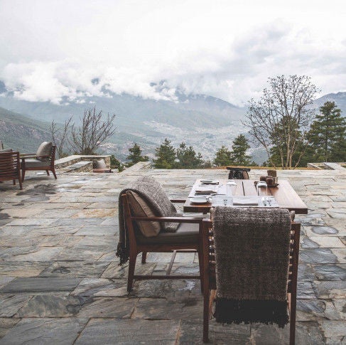 Luxurious stone lodge nestled in Bhutanese mountains, featuring traditional architecture, wooden balconies and panoramic valley views